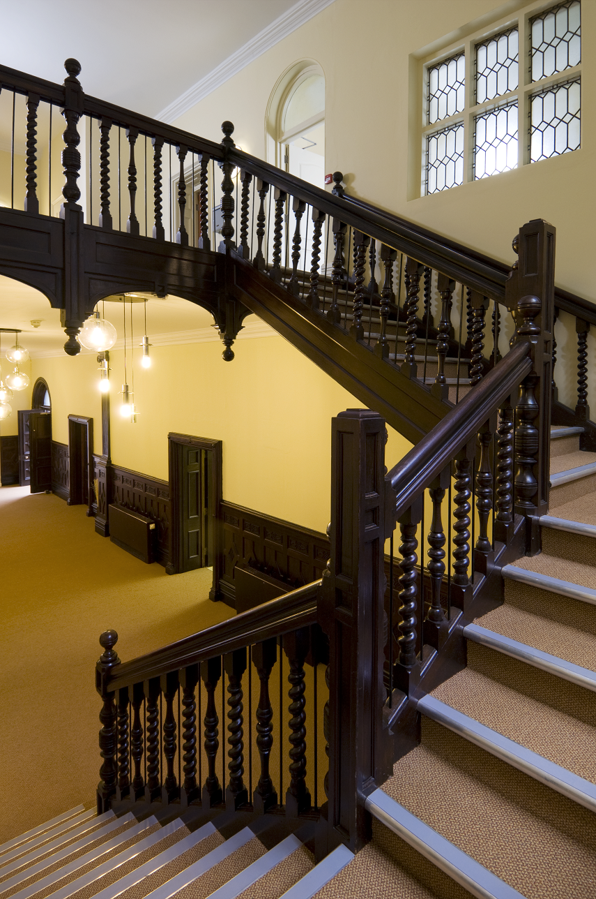 A communal hallway and stairs. The carpet is beige and the banisters are dark brown.
