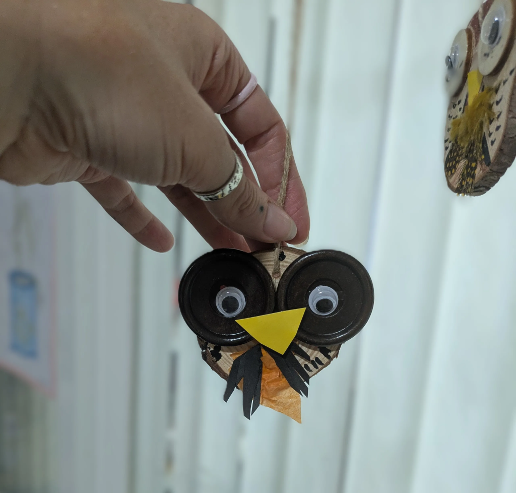 Picture of a hand holding a hand-crafted owl made out of wood and paper