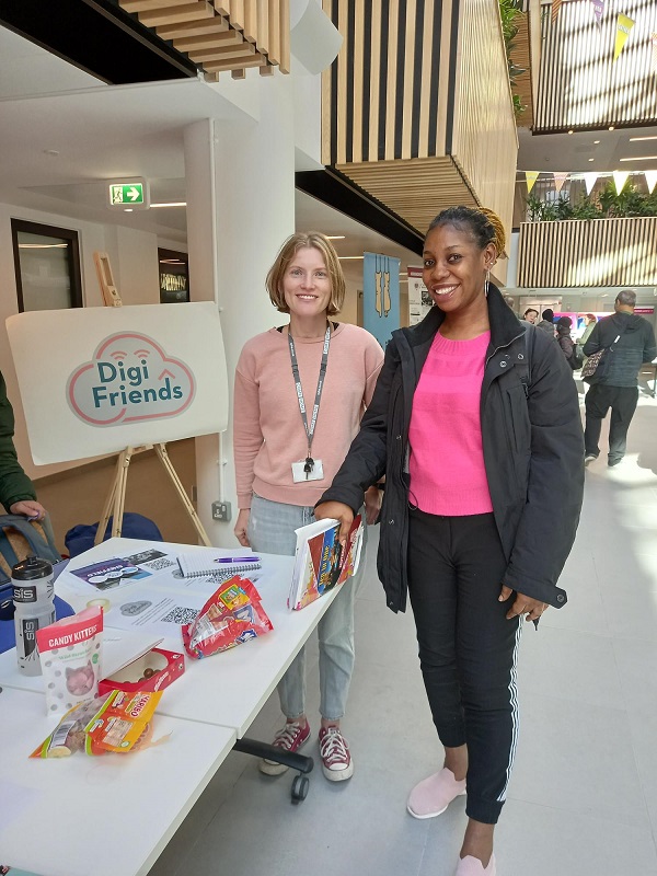 Two smiling people stood in front of a 'Digi Friends' sign at a volunteering event.