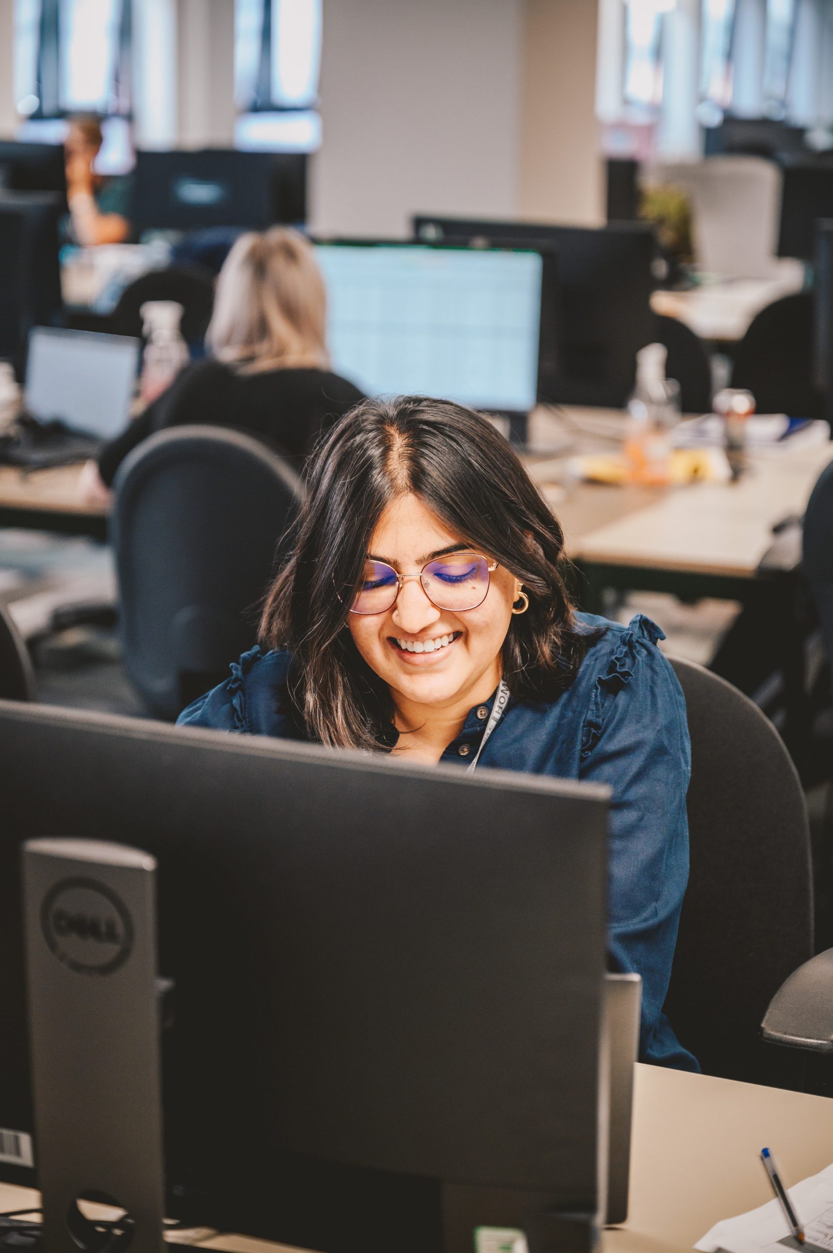 Anokhee, sat smiling at a desk in front of a computer.