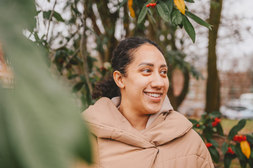 Nicole, stood by a tree, smiling and looking off-camera into the distance