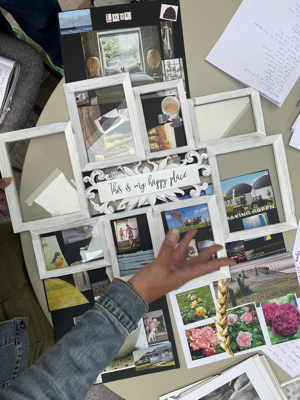 A hand in front of a photo frame filled with some images. The central image contains text that says 'this is my happy place'.