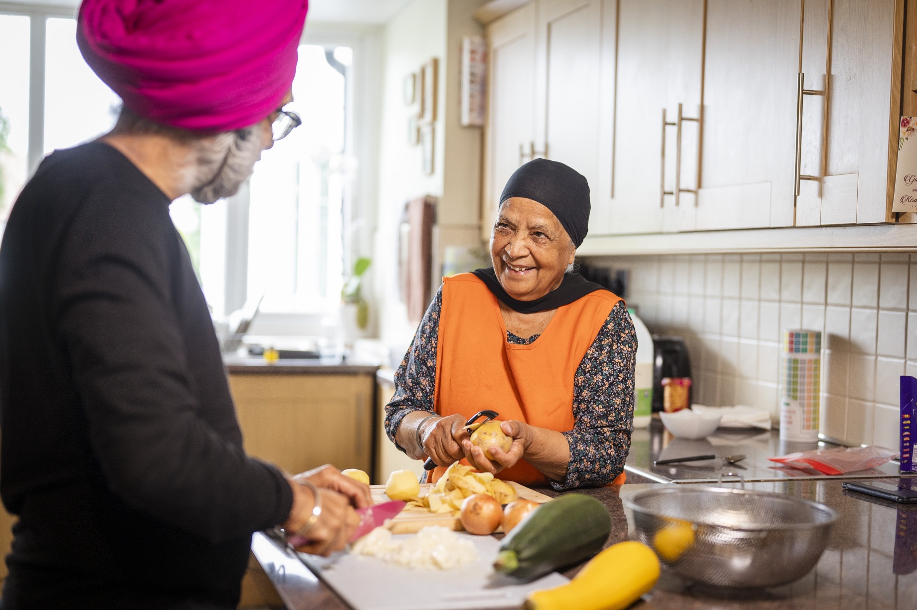 Two older people in a kitchen, preparing vegetables. You can see the lady's face, and she is smiling.