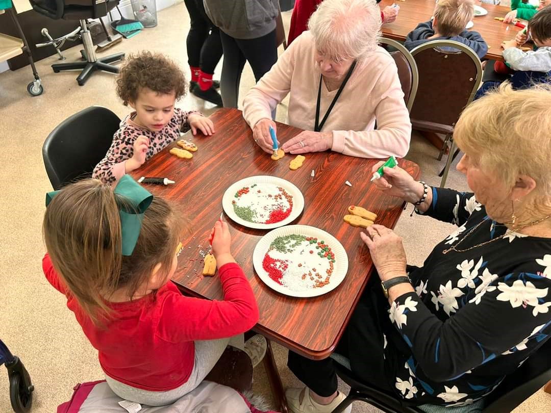 Two older women and three young children sat around a table decorating gingerbread men.